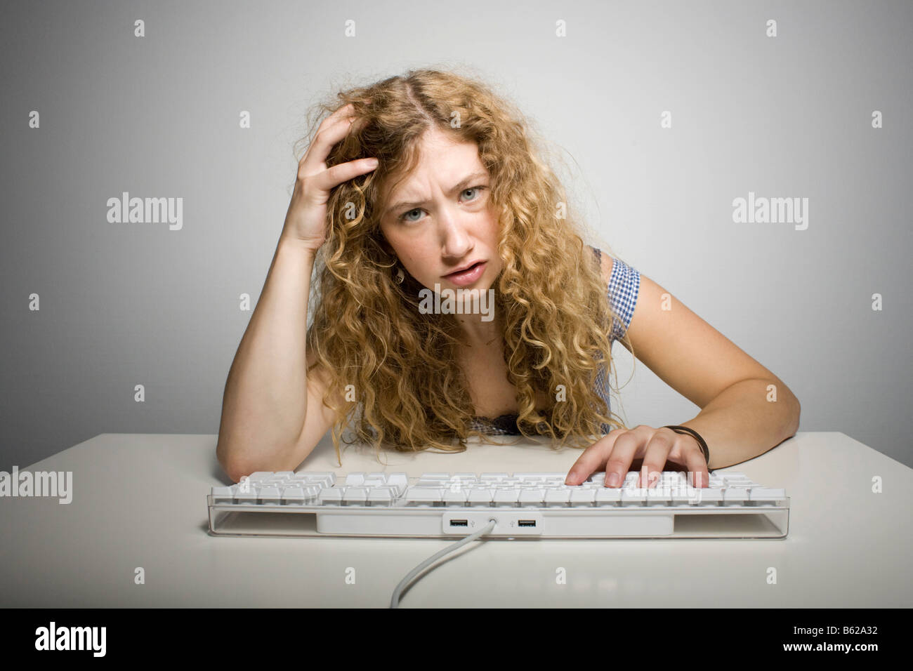Young woman with long hair sitting frustrated behind a computer keyboard on a table Stock Photo