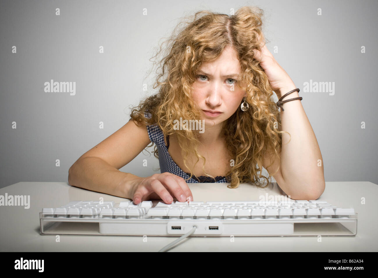 Young woman with long hair sitting frustrated behind a computer keyboard on a table Stock Photo