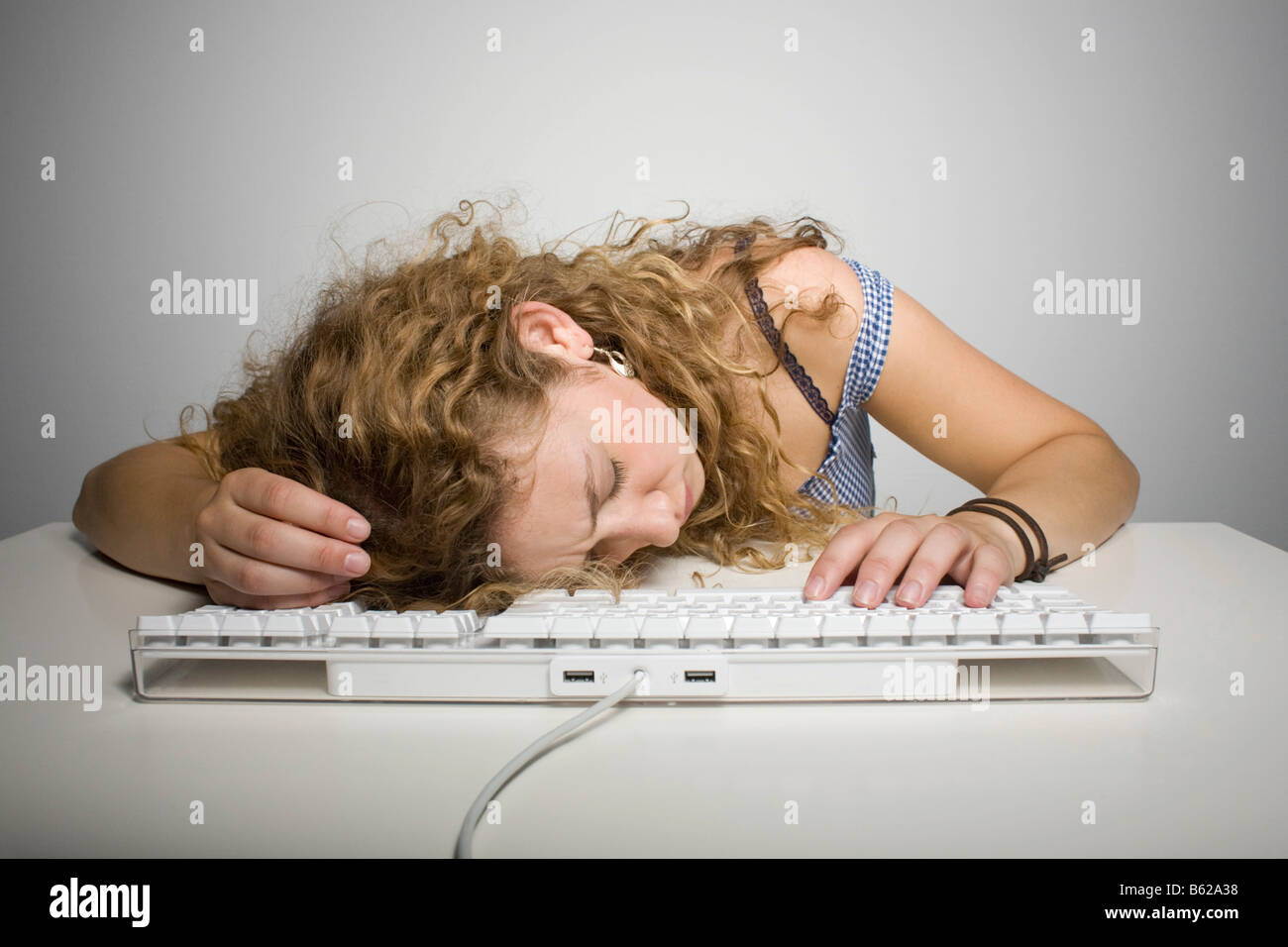 Young woman with long hair resting her head on a computer keyboard on a table Stock Photo