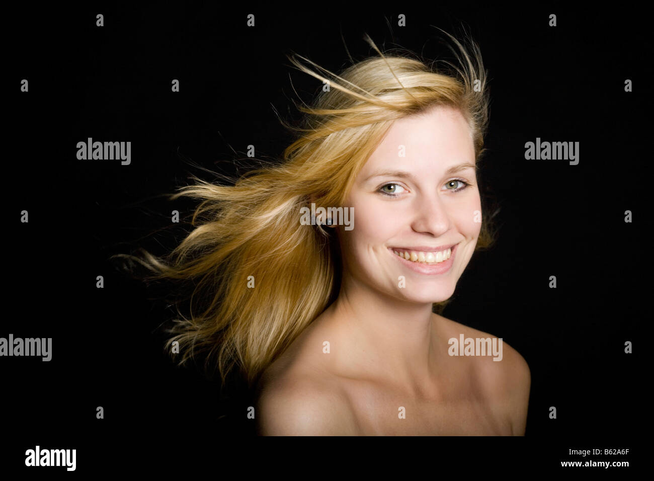 Young blond woman with long blowing hair in front of black Stock Photo