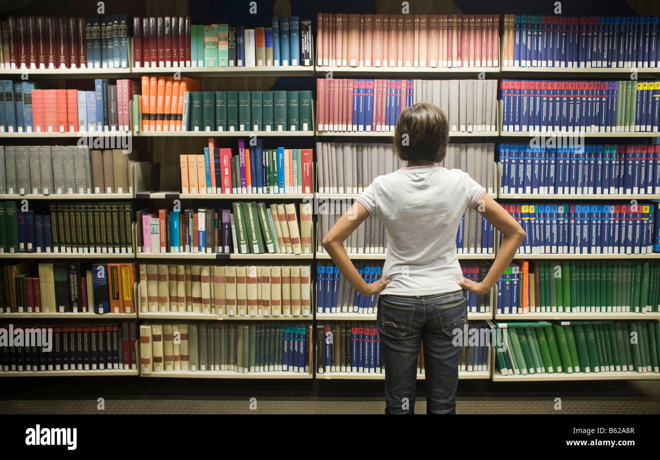 Young dark-haired female student standing in front of a bookshelf in a ...