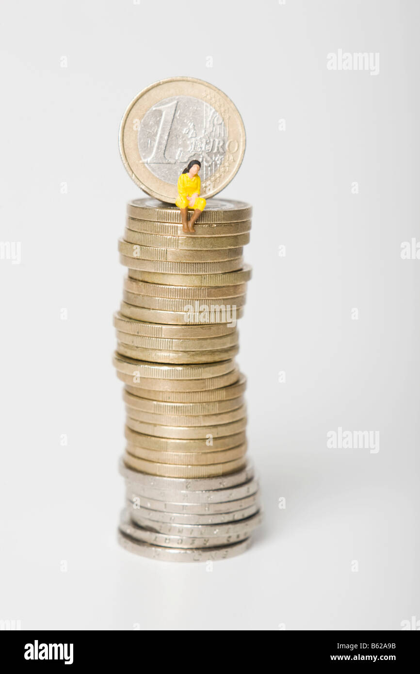 Woman figure wearing a yellow dress sitting on a pile of euro coins, symbolic for savings or consumption Stock Photo