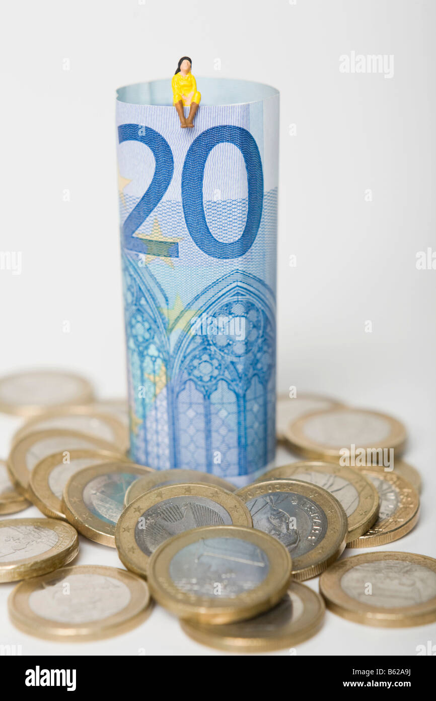 Woman figure wearing a yellow dress sitting on a 20 euro note, euro coins scattered around them, symbolic for savings or consum Stock Photo