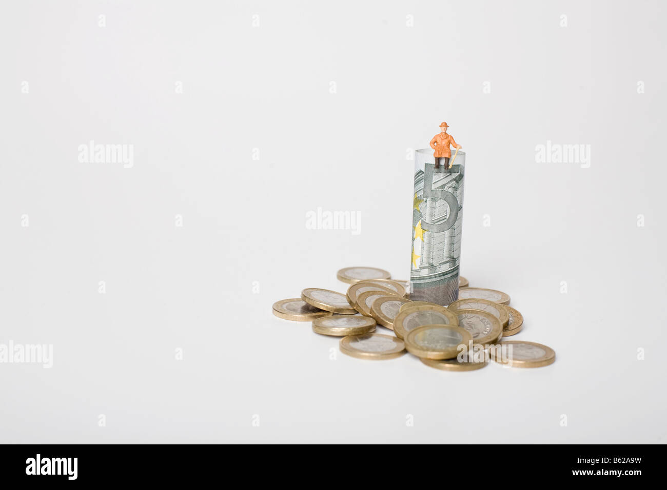 Pensioner figure sitting on a 5 euro note, euro coins scattered around them, symbolic for family budget Stock Photo