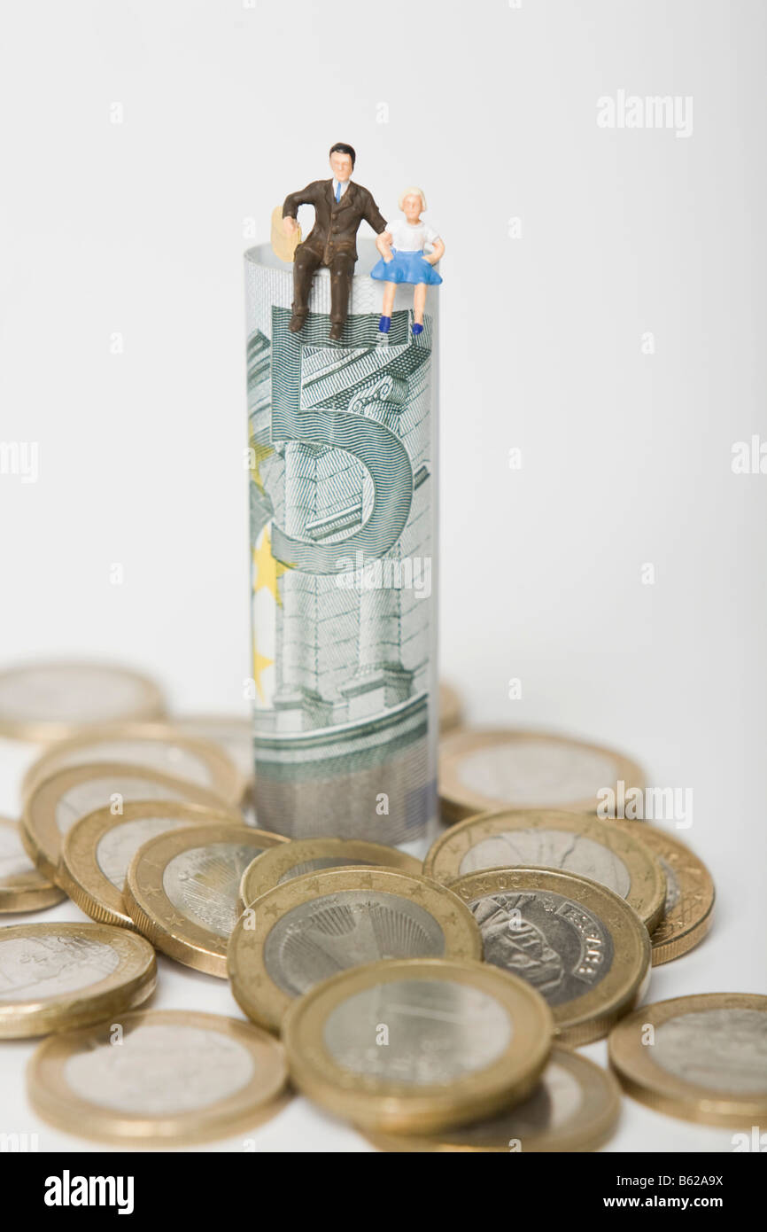 Father and daughter figures sitting on a 5 euro note, euro coins scattered around them, symbolic for family budget Stock Photo