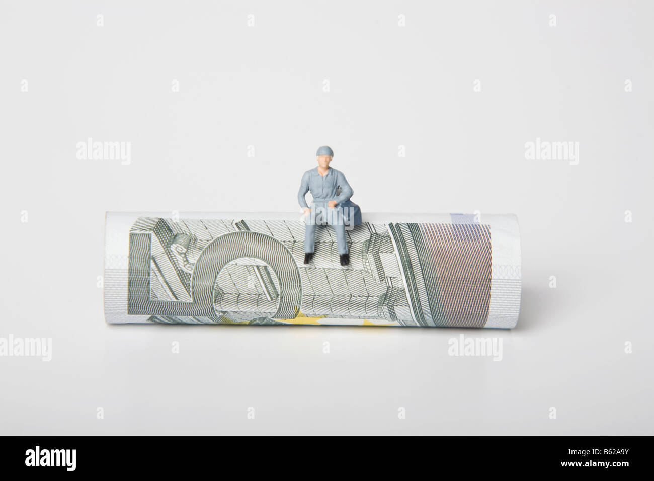 Worker figure sitting on a 5 euro note, euro coins scattered around them, symbolic for wage Stock Photo