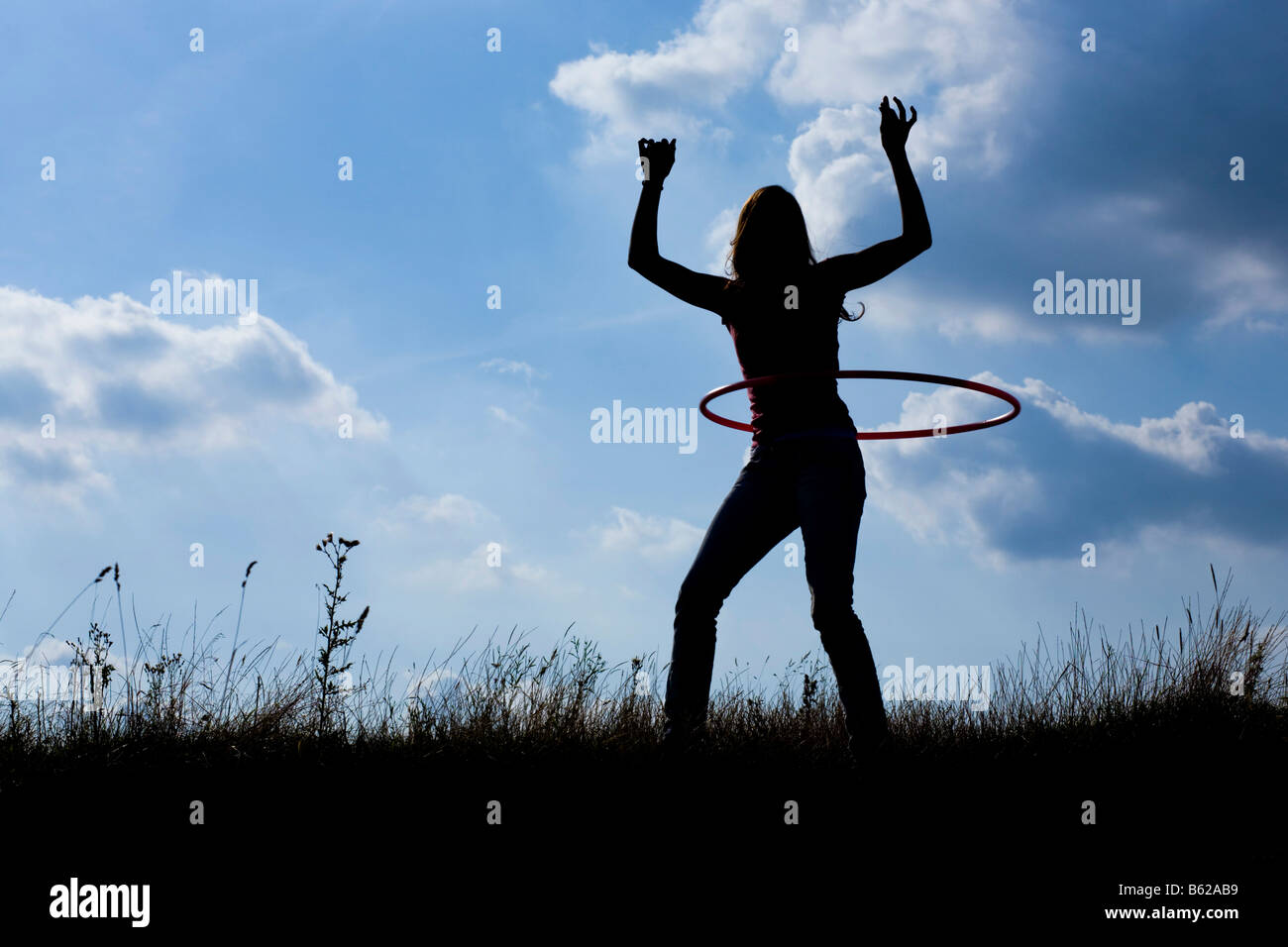 Silhouette of a young woman with a hula hoop in front of a cloudy sky Stock Photo
