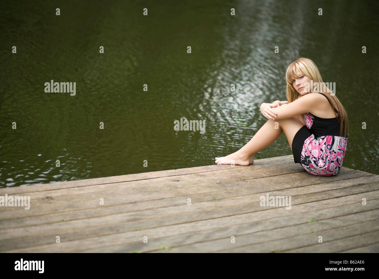 Young blonde woman sitting on a jetty by the water Stock Photo