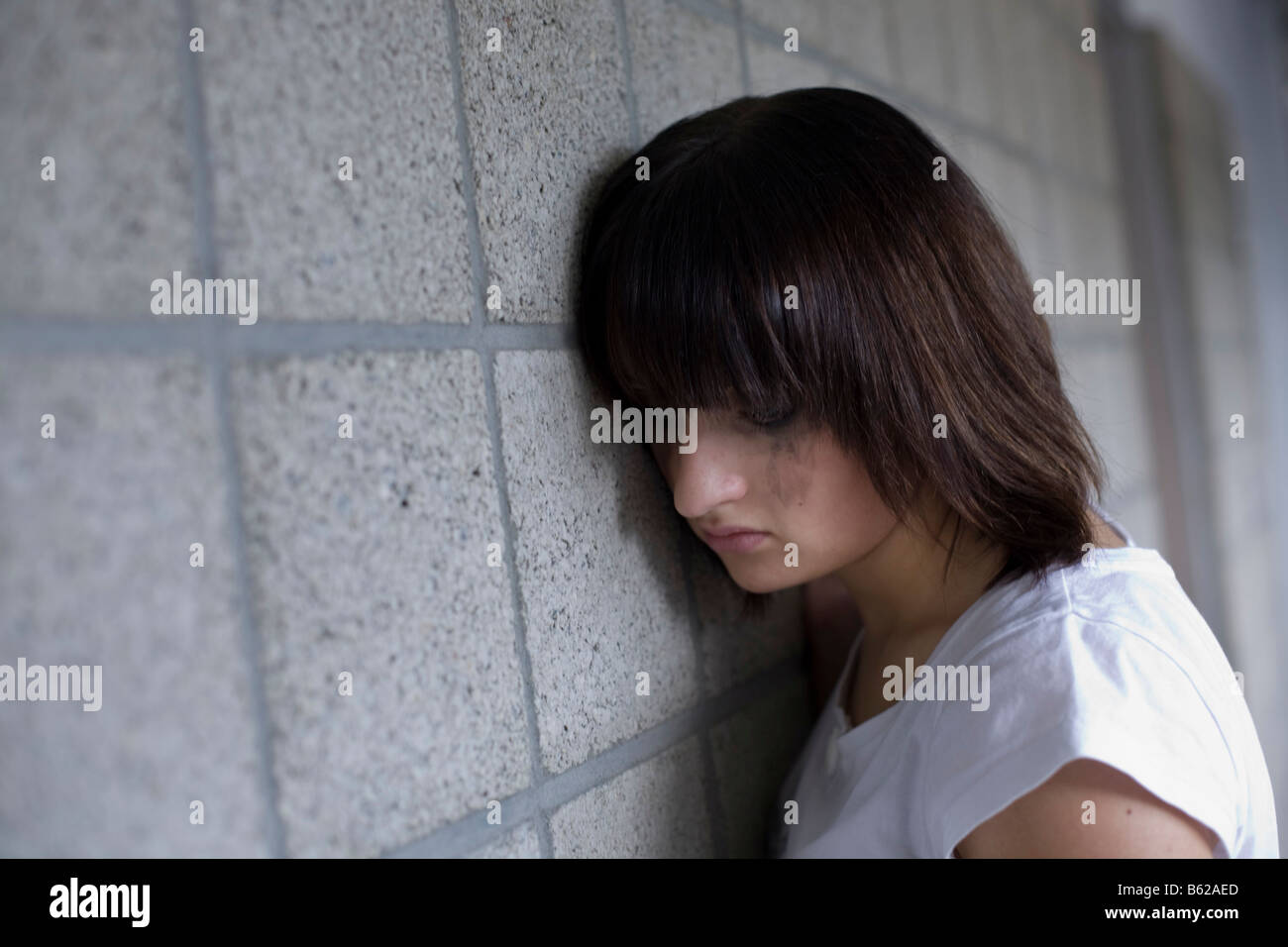 Sad young woman leaning against a wall Stock Photo