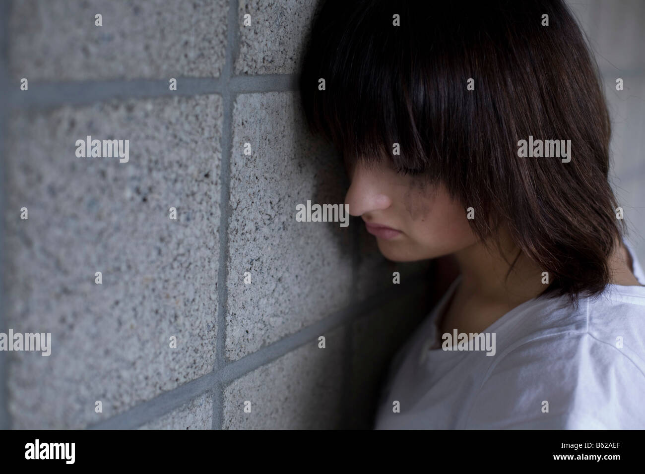 Sad young woman leaning against a wall Stock Photo