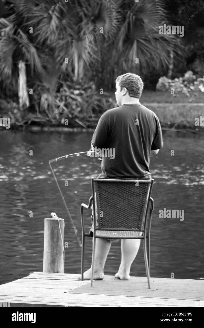 young boy with fishing pole on dock black and white pic, barefooted looking over water Stock Photo