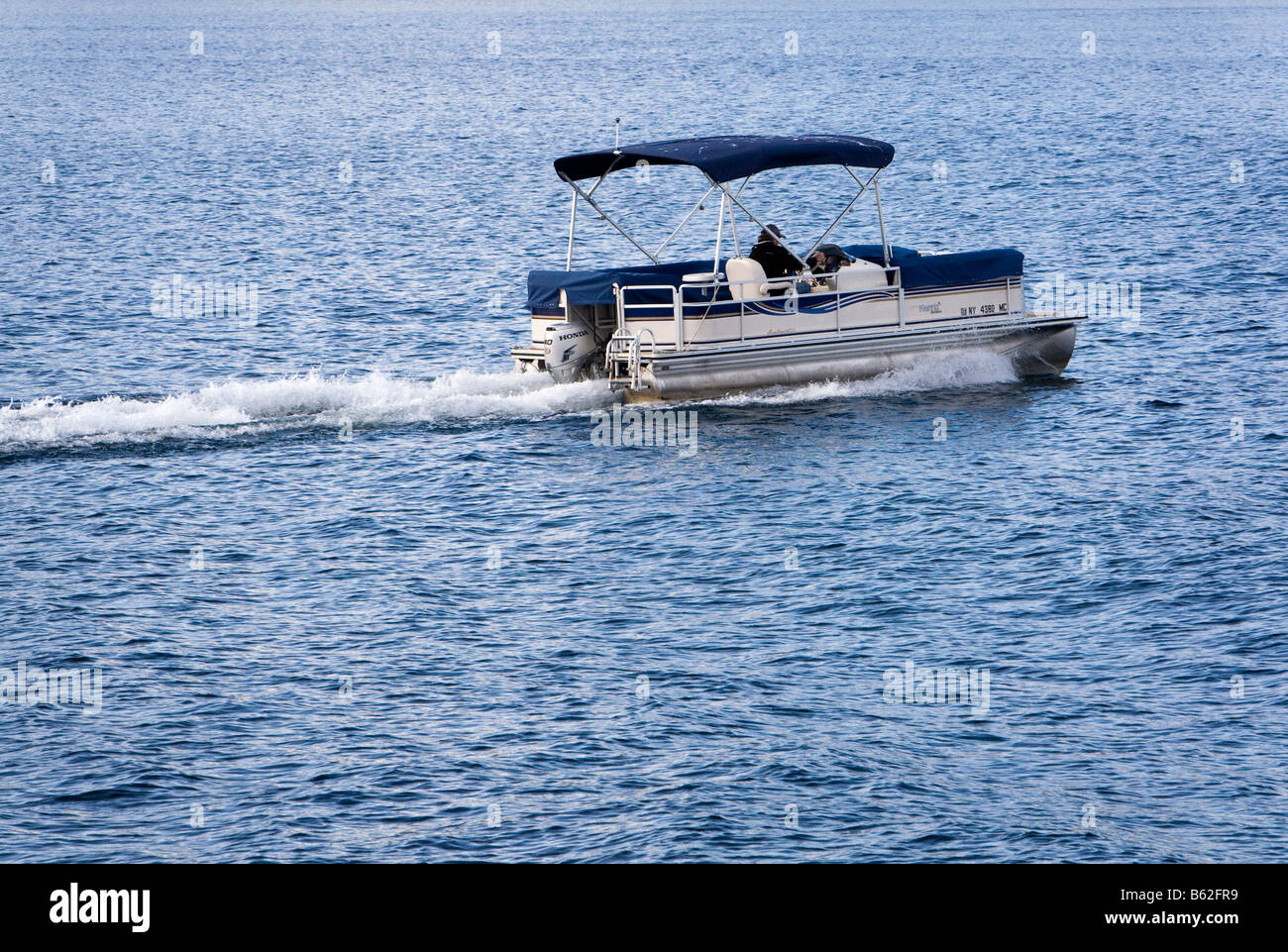 A pontoon deck boat motoring across Lake in Adirondack State Park New York Stock Photo