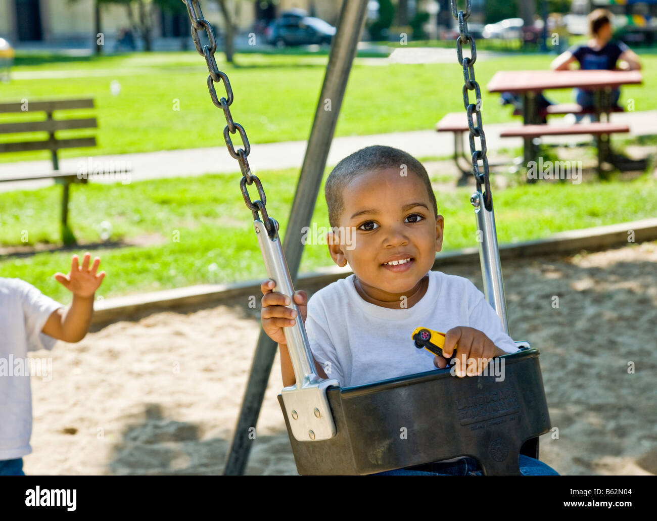 African-American male toddler being pushed on the swing set by his 4 year old brother on a city playground. Stock Photo