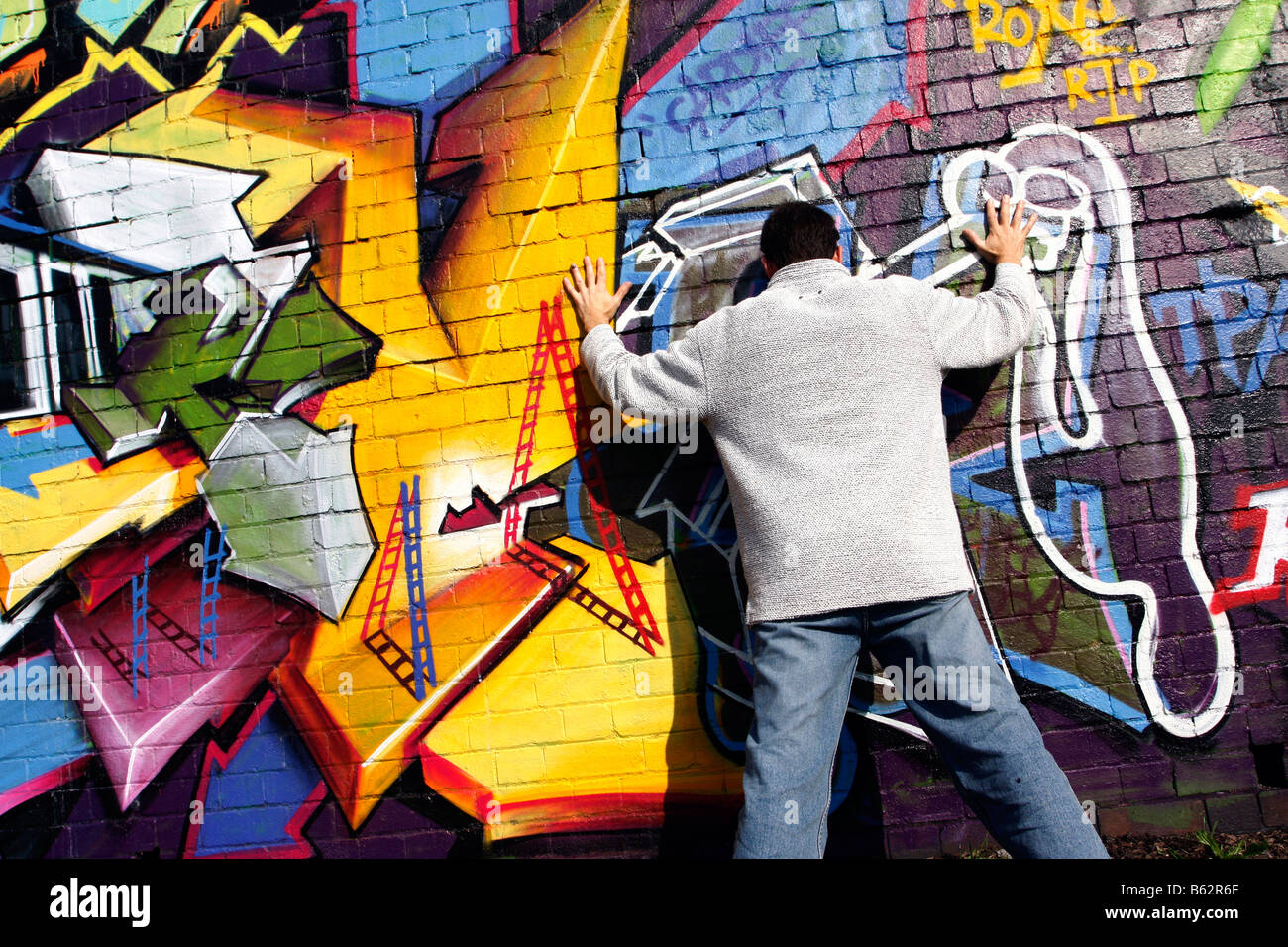 man standing against and facing a wall which has graffiti art on it graffiti spray paint brick wall art painting Stock Photo