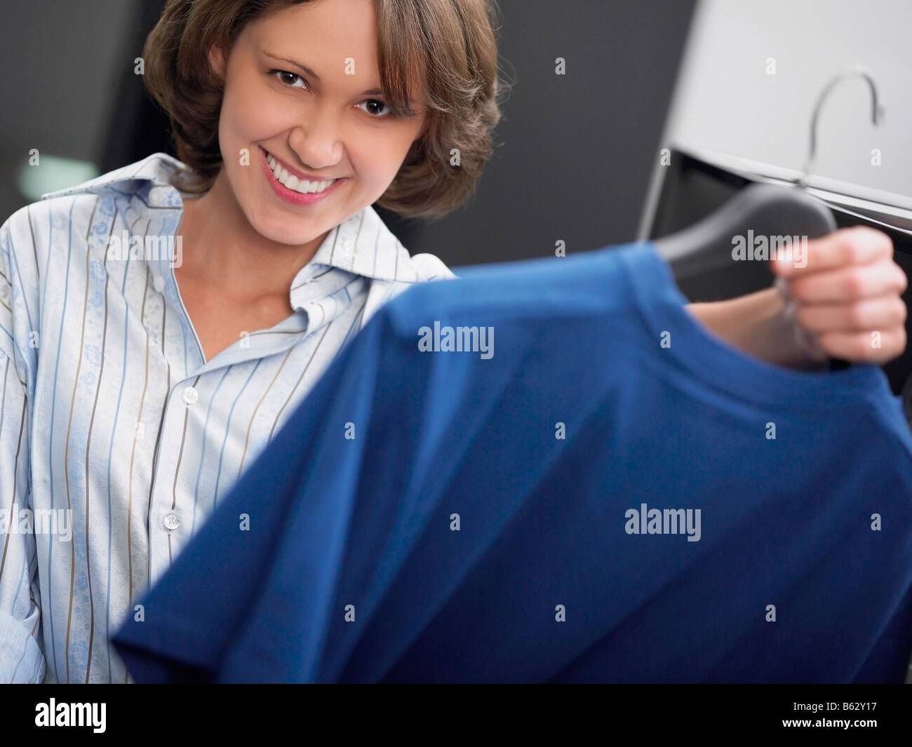 Portrait of a young woman holding a t-shirt on a hanger and smiling Stock Photo
