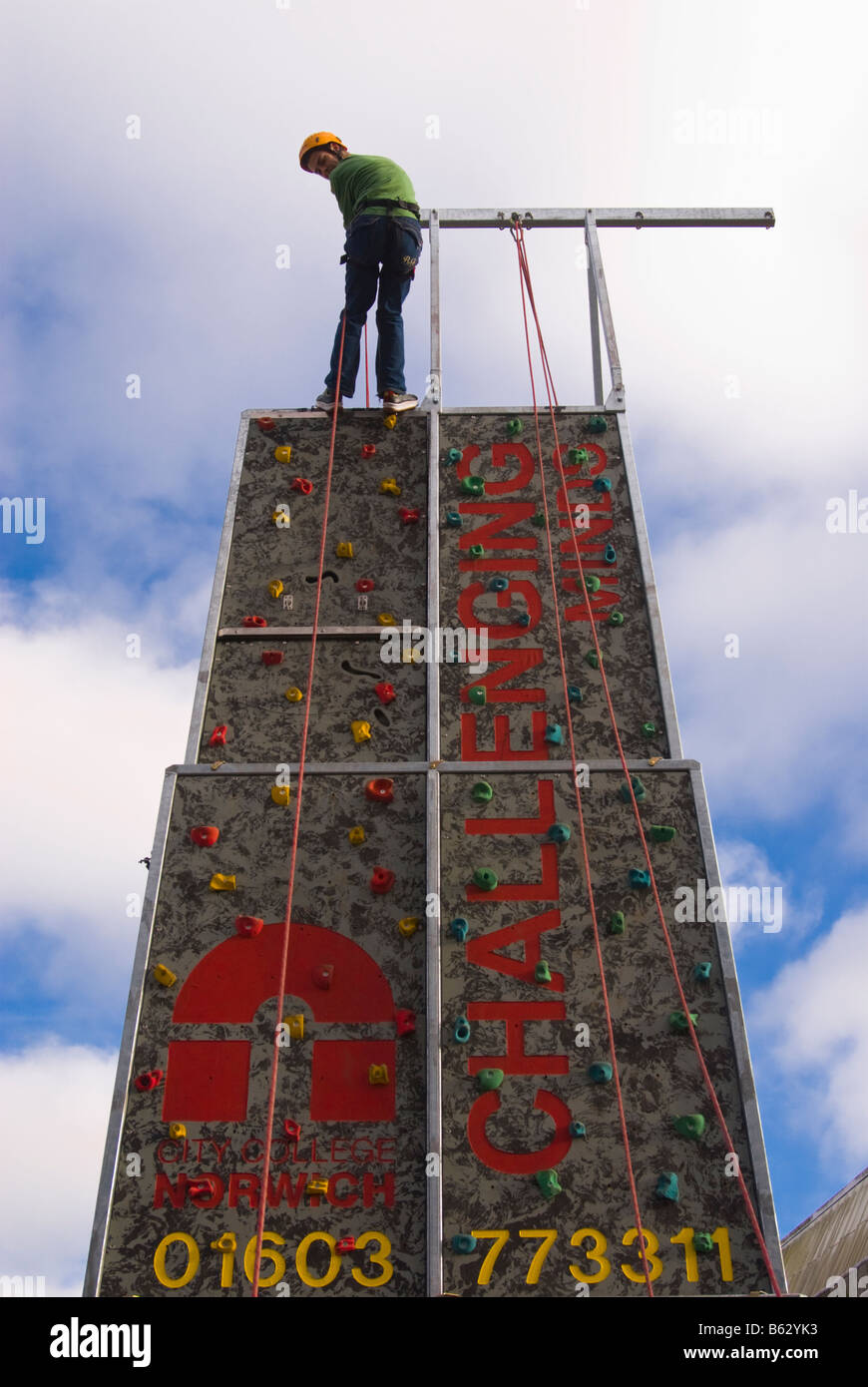 Person climbing up man made rock wall with safety harness and helmet to