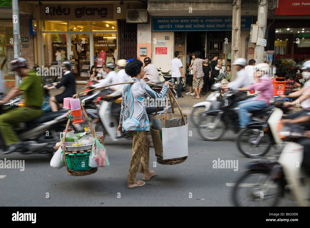 Vietnamese street trader walks across the street through the blur off busy traffic in chaotic Ho Chi Minh City, Vietnam Stock Photo