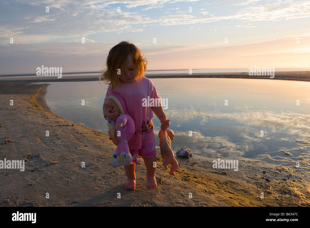 Baby girl carrying dolls on the beach Stock Photo
