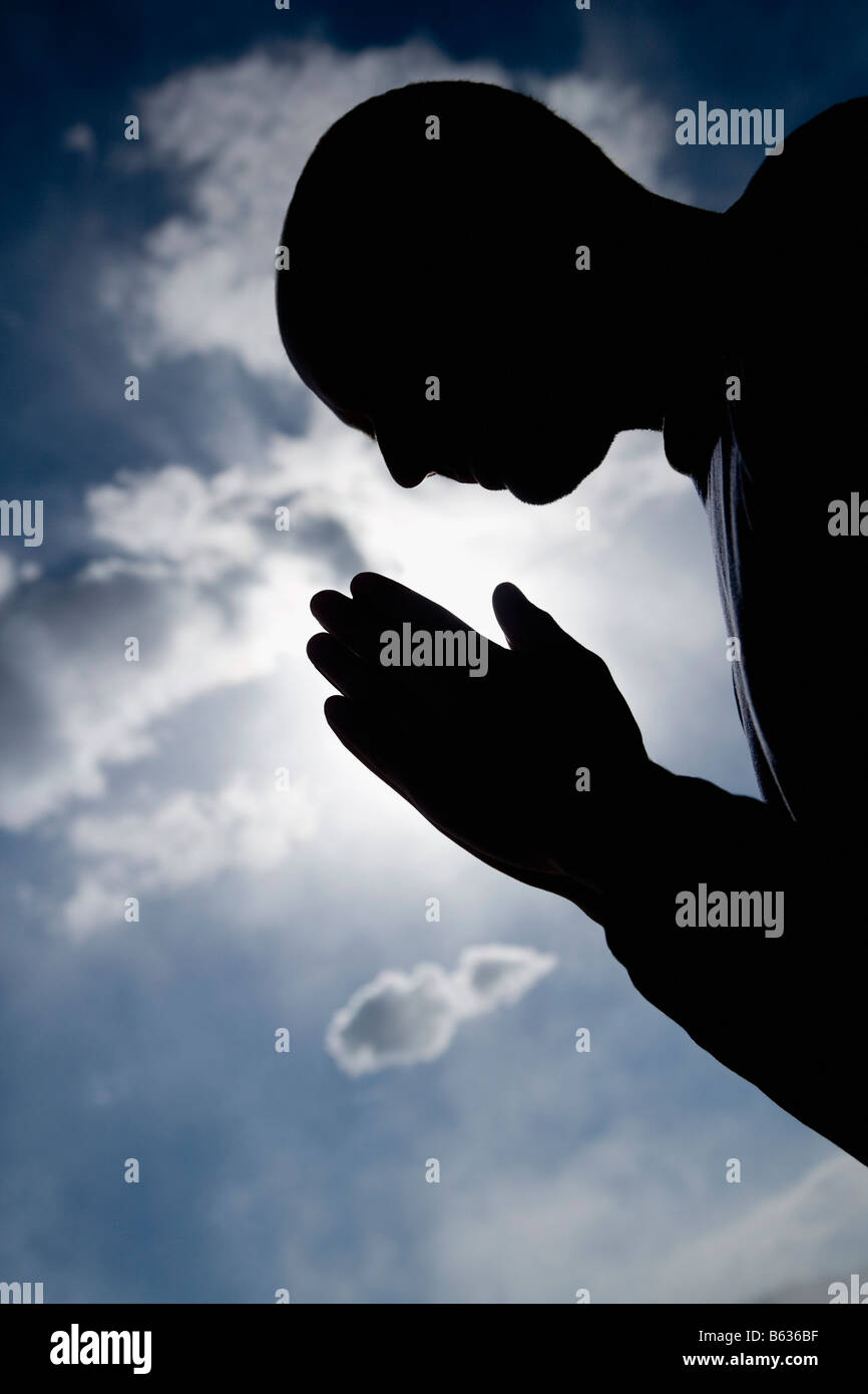Silhouette of a man in a prayer position Stock Photo
