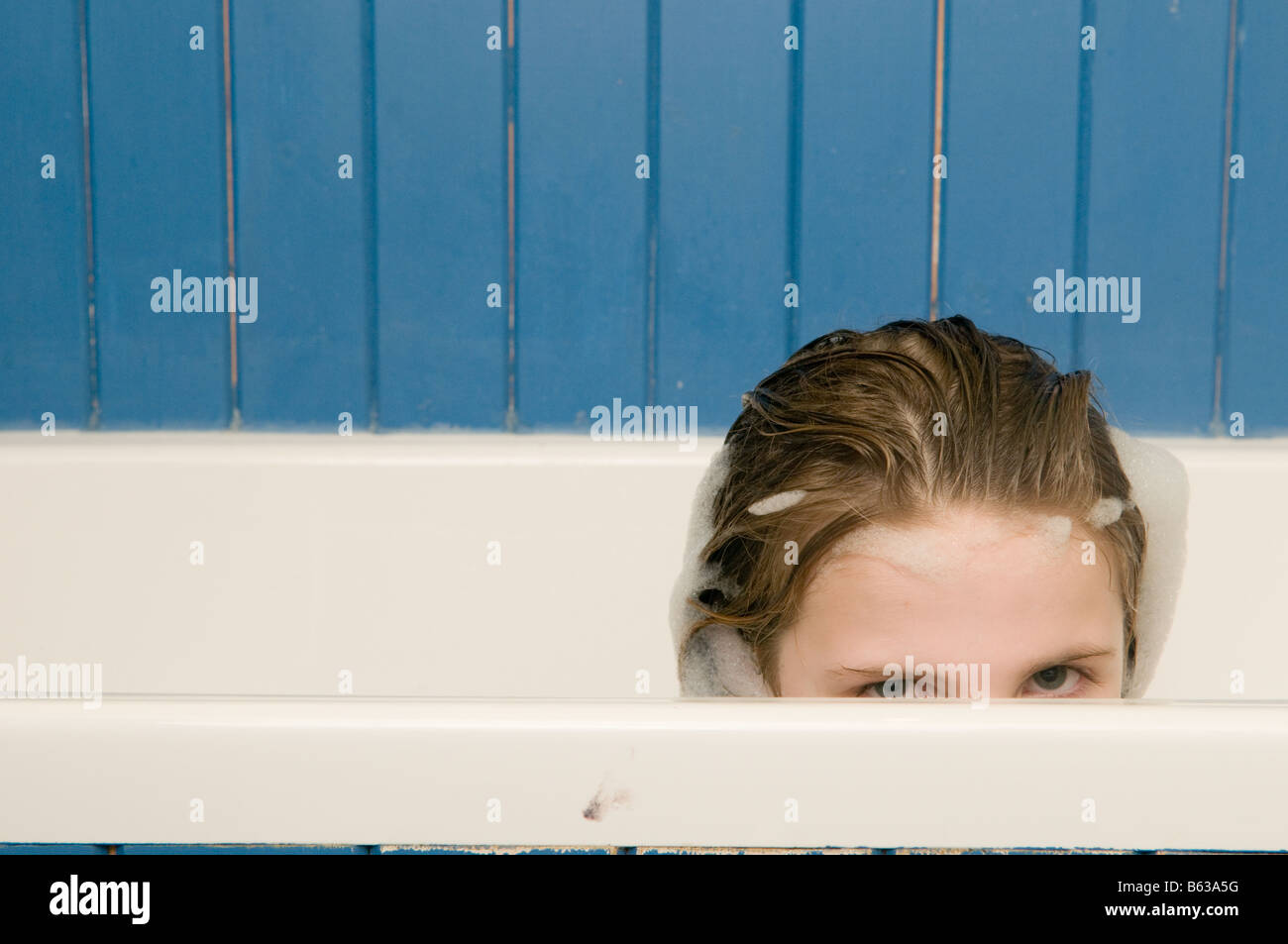 Ten year old girl in the bath peering over the edge of the bath looking
