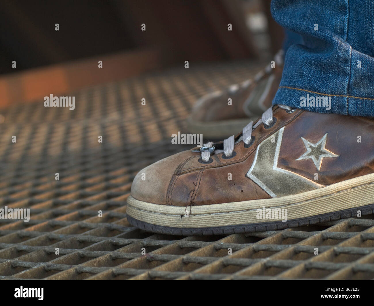Feet in Converse sneakers standing on a iron grill. Stock Photo