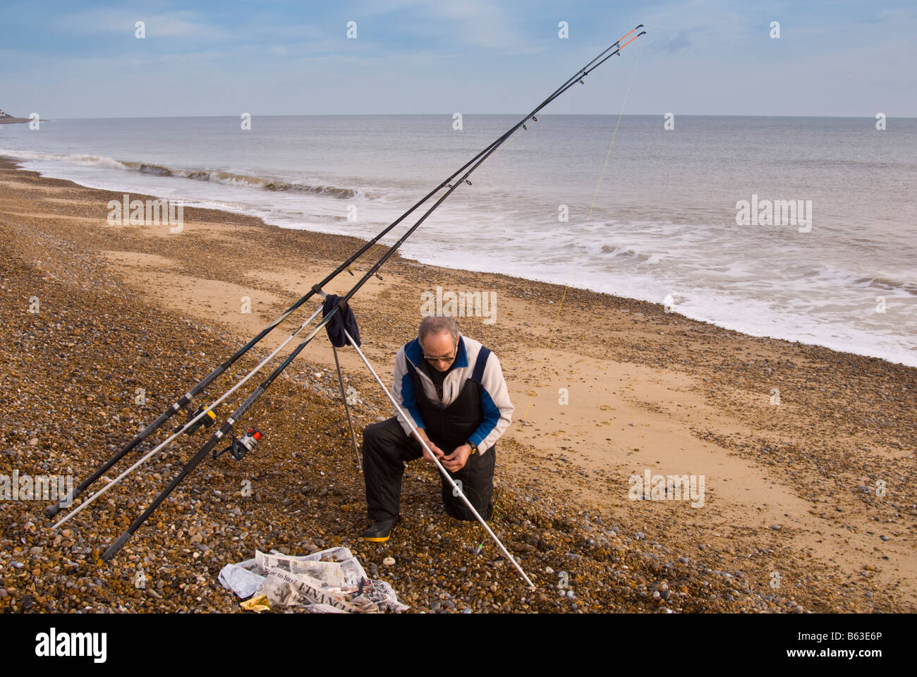 Man sea fishing with rod on a uk beach putting his bait on the hook