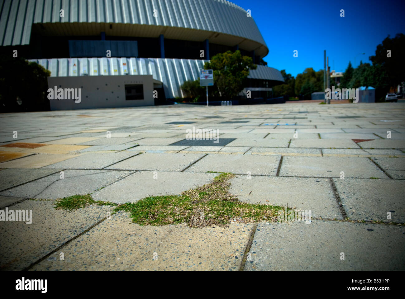 Small patch of grass growing amongst concrete, disused Perth Entertainment Centre in background. Perth, Western Australia Stock Photo