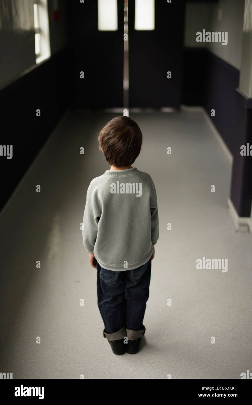 Six year old boy stands alone in school corridor Stock Photo