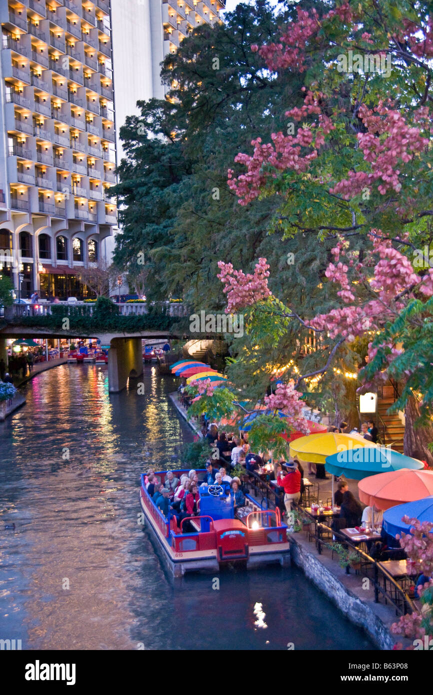 San Antonio Riverwalk with Rio San Antonio Cruises dining cruise on San Antonio River in evening, Hilton Hotel in background Stock Photo