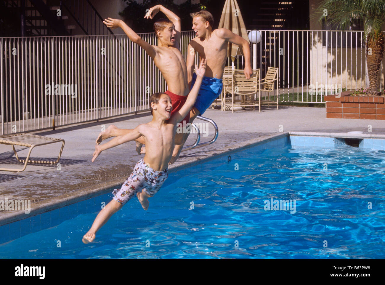 Three white boys jump from side of pool into water. Stock Photo