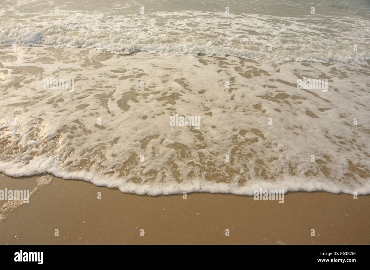 The white foam of gently breaking waves makes a wavy line at a sandy