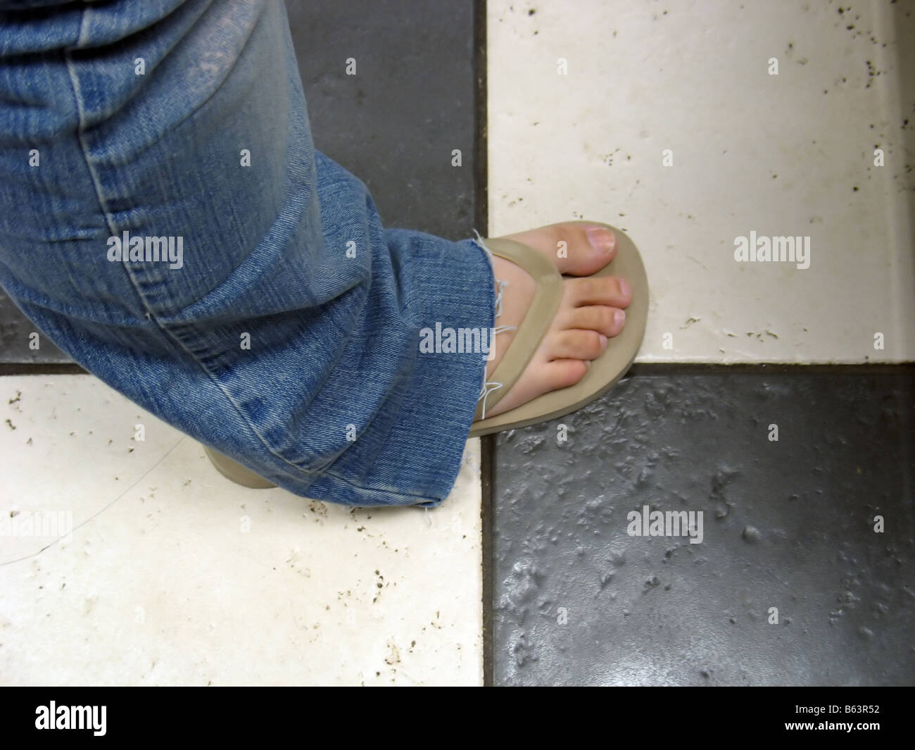 a flip flop on a girl s foot standing on a ceramic tile floor Stock Photo