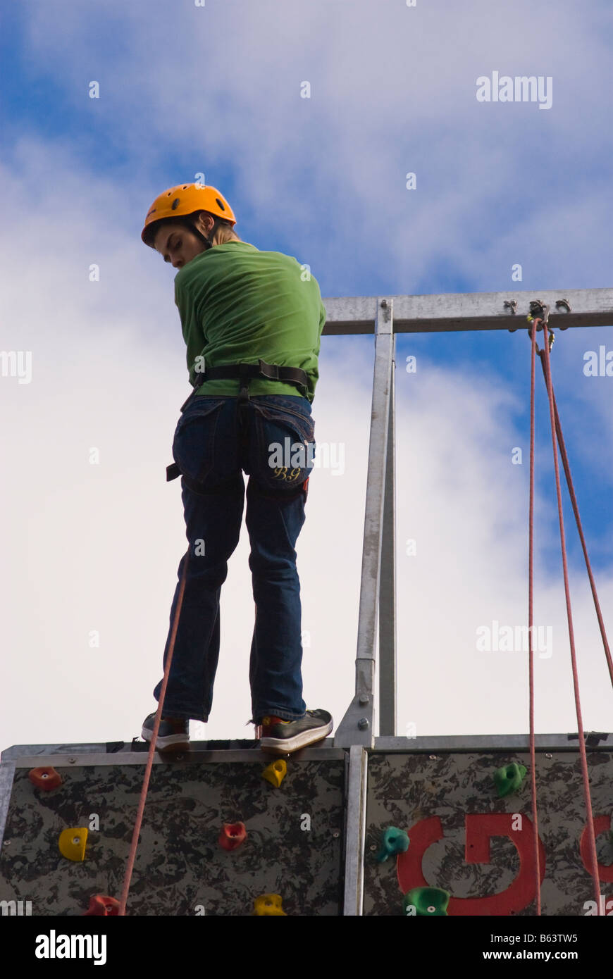Person climbing up man made rock wall with safety harness and helmet to