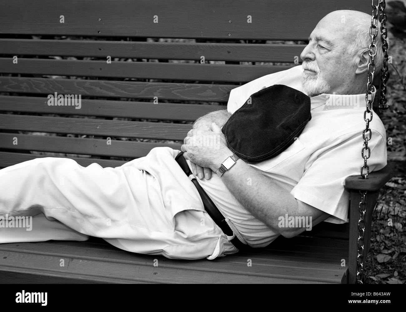 Black and white image of senior man taking a nap on a park swing Stock Photo