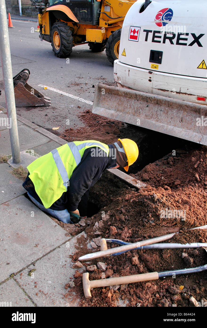 A workman in the process of clearing a hole under the pavement in order to lay new pipes. Stock Photo