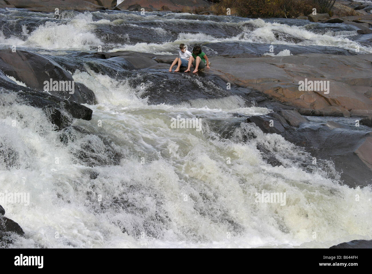 children relaxing on rocks by raging river rapids Stock Photo