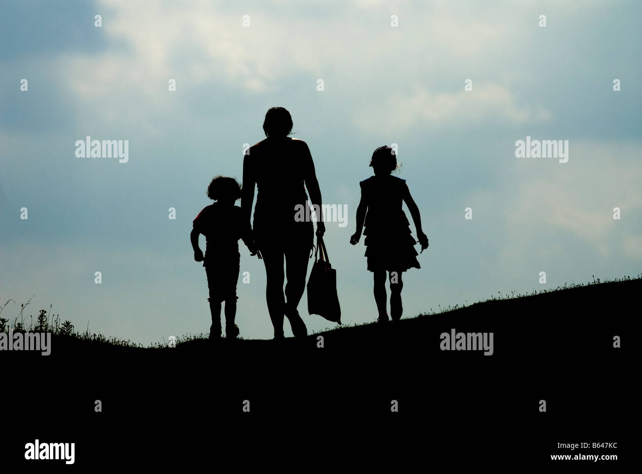 A mother and two young girls walking in the countryside.  Silhouette. Stock Photo