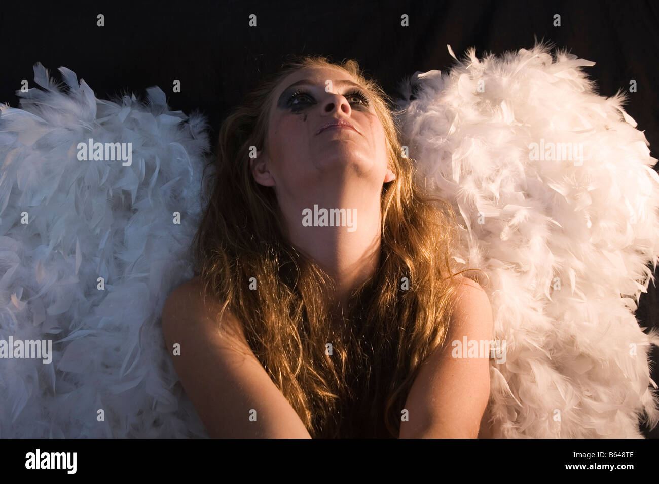 Young woman with ruined black eye make up wearing white angel wings Stock Photo