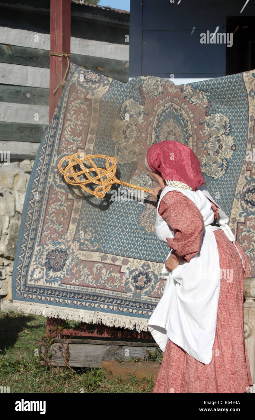 An older woman beating the dirt from an old wool rug on her homestead porch Stock Photo
