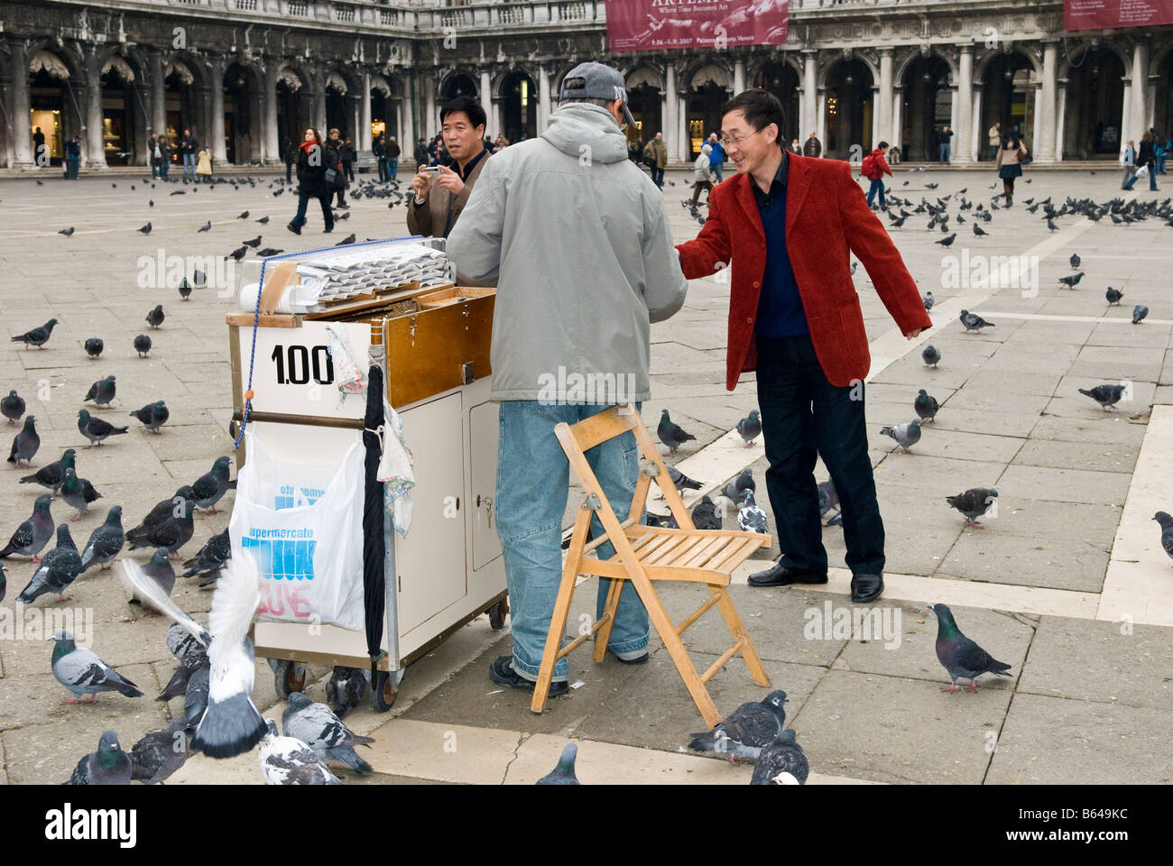 Man selling pigeon food to Asian tourists on St. Mark's Square, Piazza San Marco Venice Italy Stock Photo