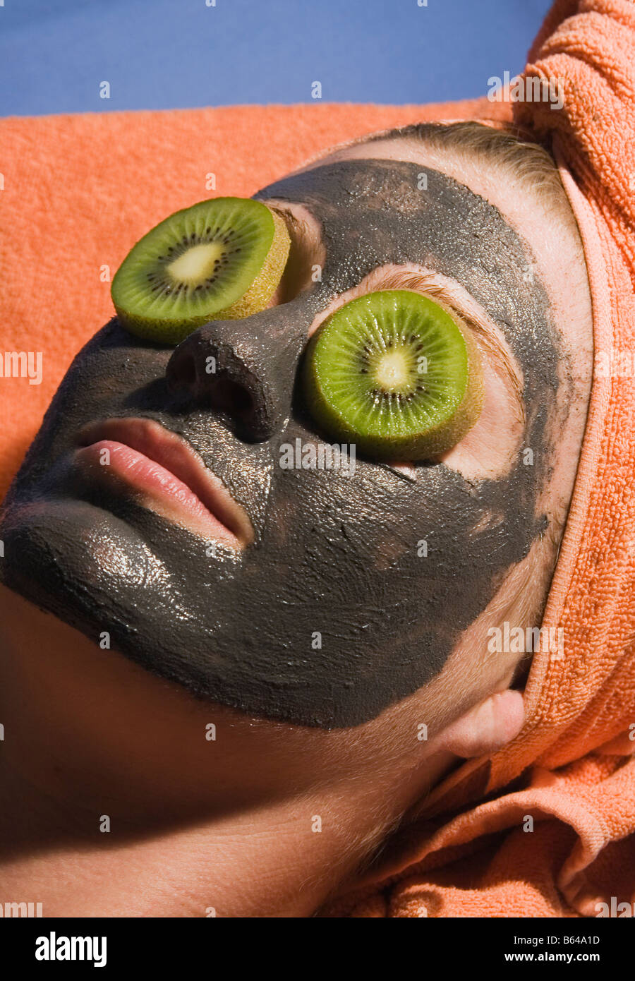 Young woman with exfoliating face mask and slices of kiwi fruit on her eyes Stock Photo