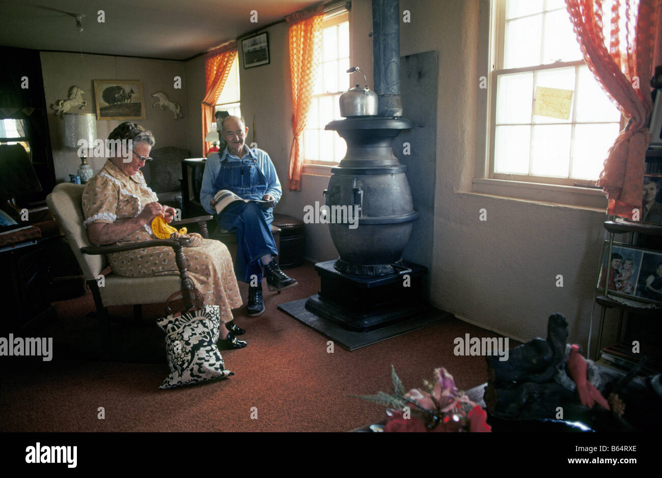 An elderly farm couple sit in front of their wood burning stove in