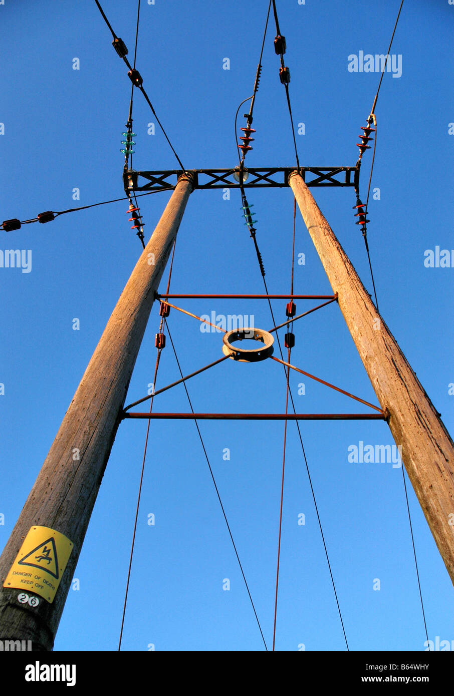 Looking up at an electric pylon - A danger sign is present on the base of one of the poles. Stock Photo