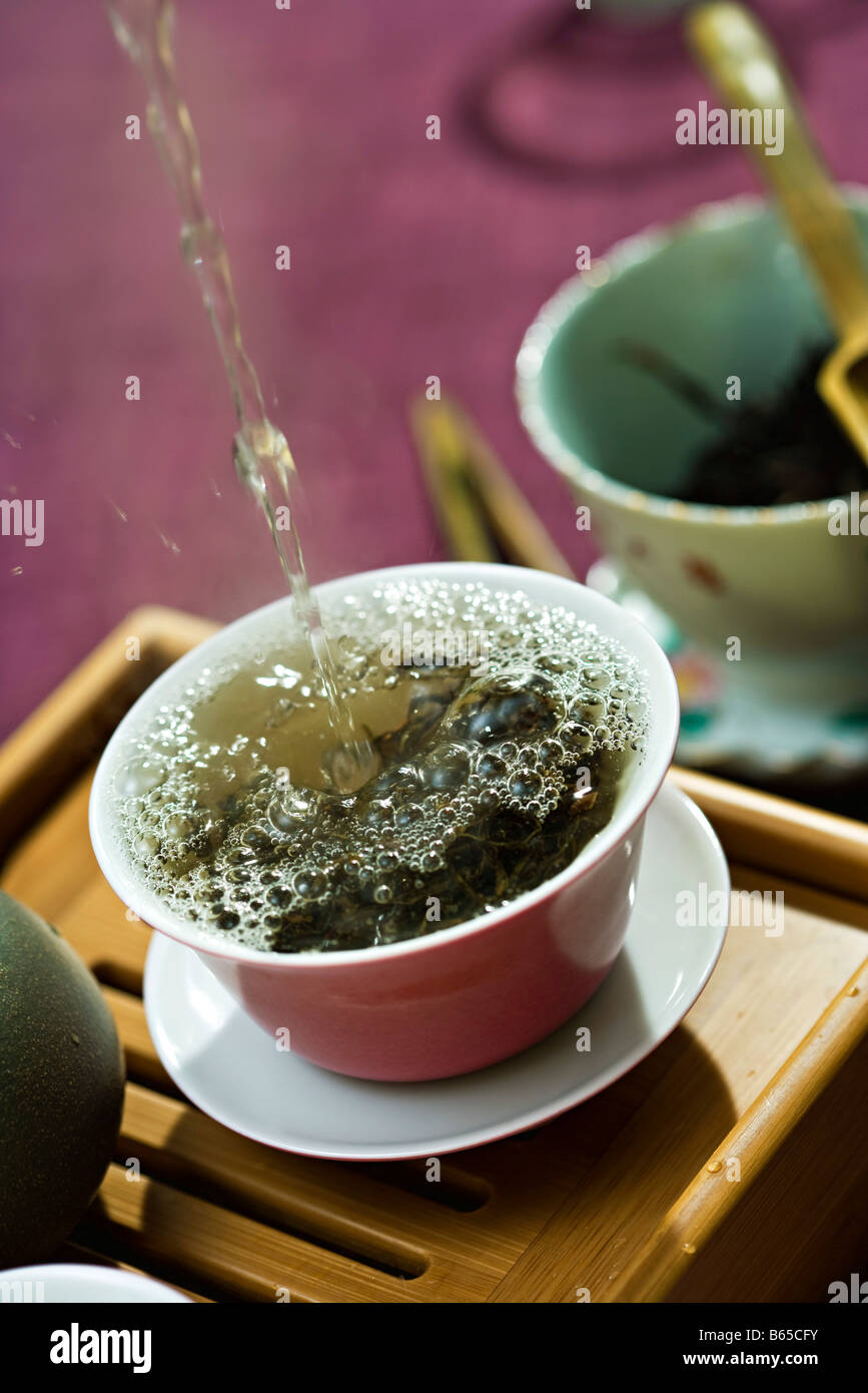 Hot water being poured and splashing over tea leaves in tea cup Stock Photo