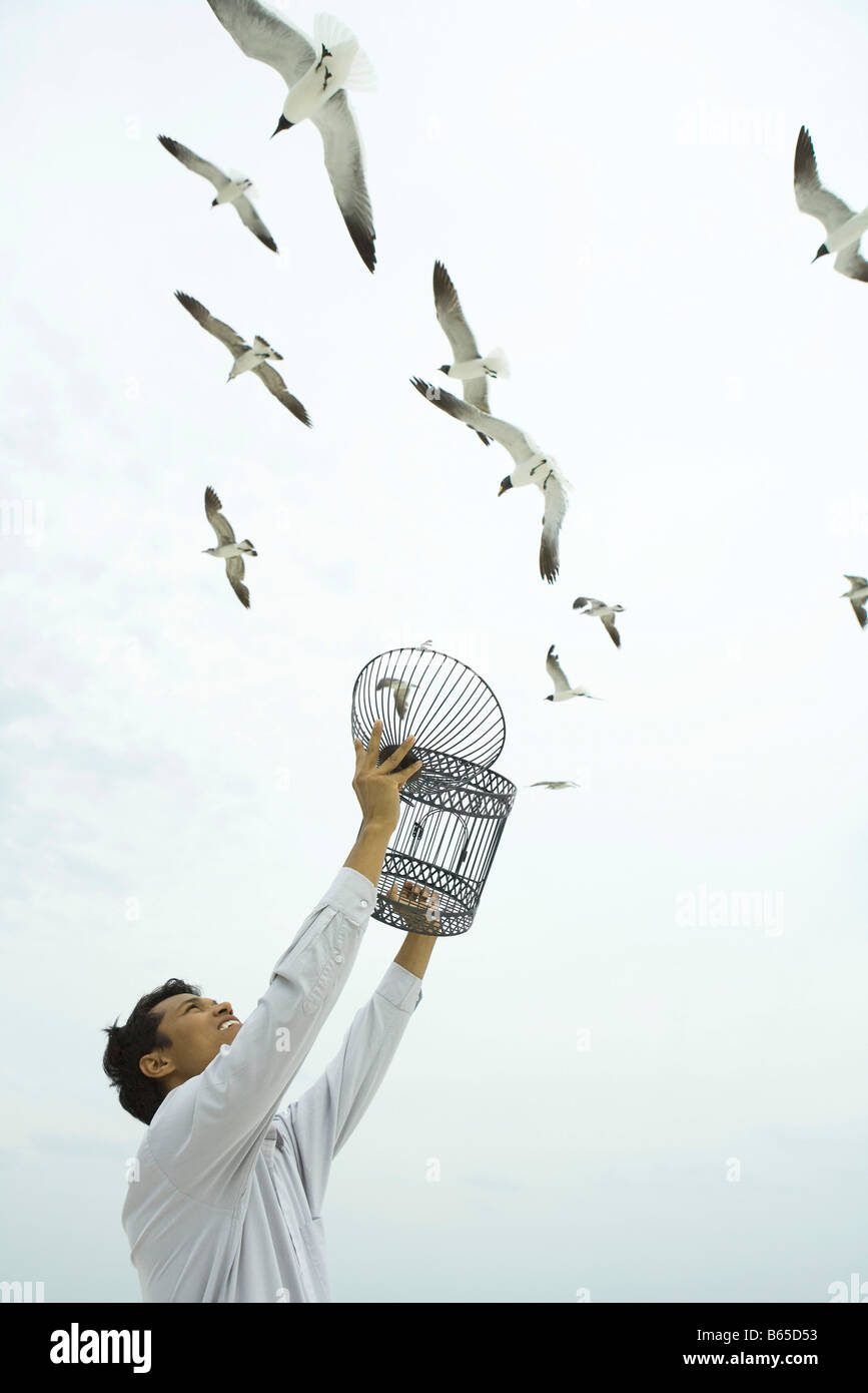 Man holding up empty birdcage, birds flying overhead Stock Photo - Alamy