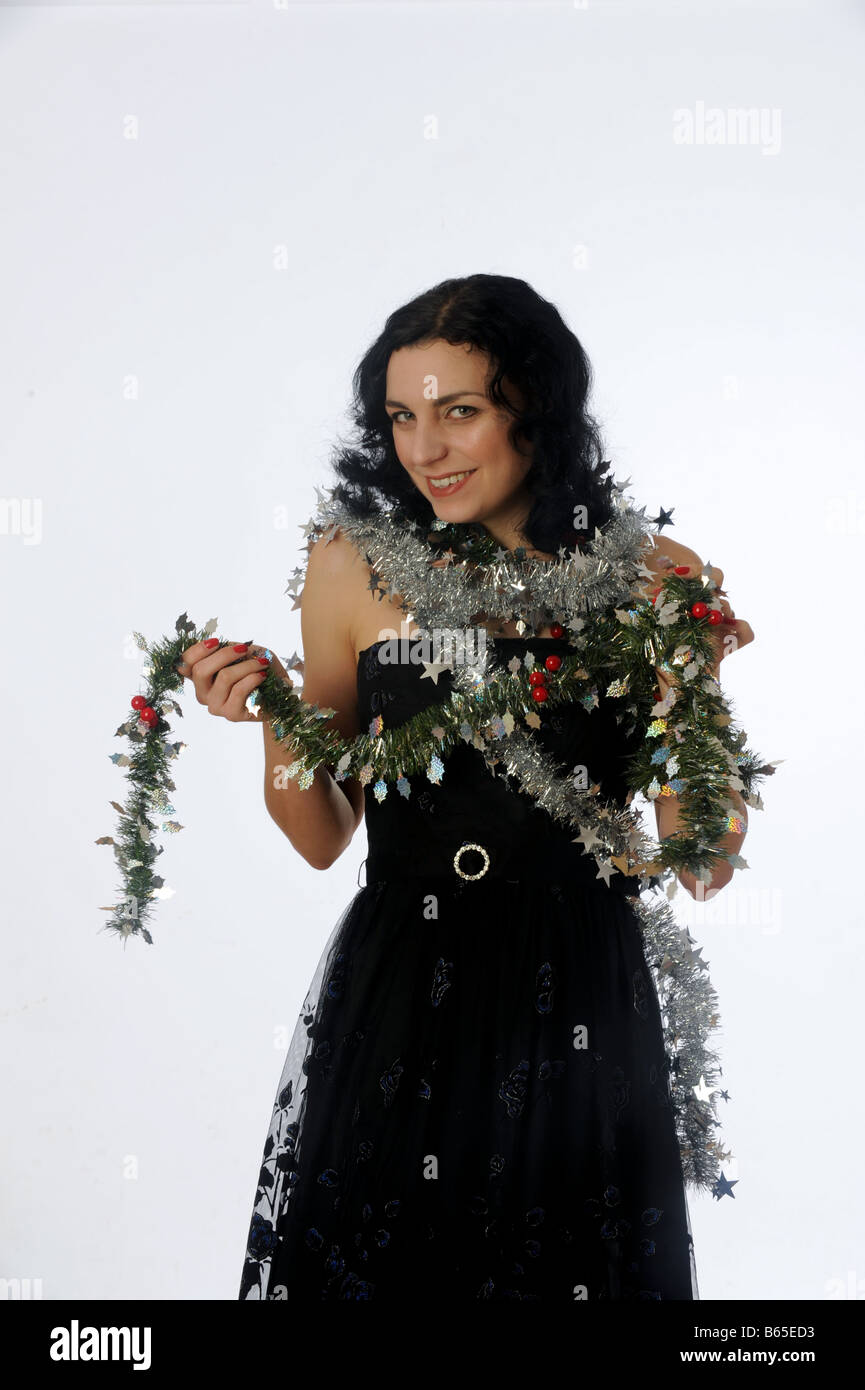Woman with dark hair and black dress wrapped in Christmas tinsel and  decorations Stock Photo