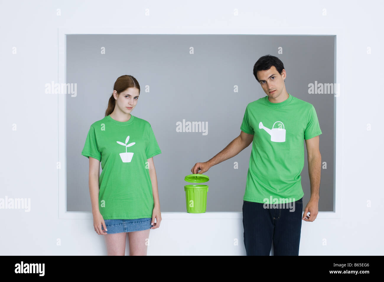 Young adults wearing tee-shirts printed with watering can and potted plant, man opening small garbage can Stock Photo