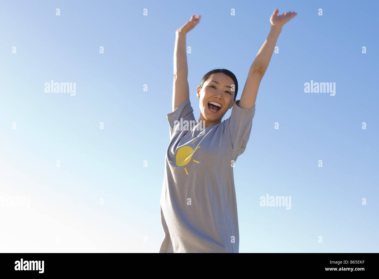 Woman with arms raised in the air, smiling at camera Stock Photo