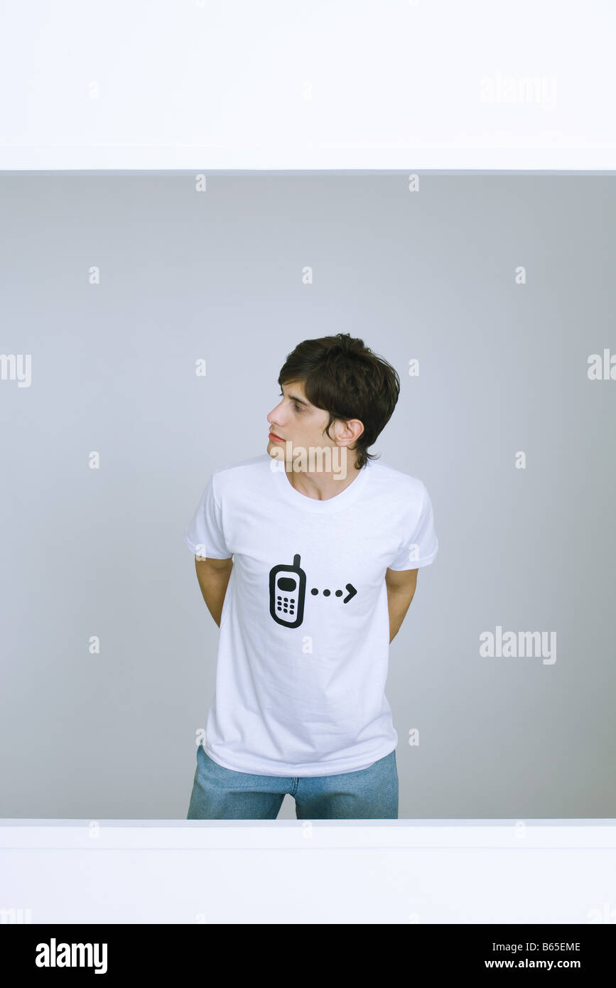 Young man wearing tee-shirt with cell phone graphic, looking away, hands behind back Stock Photo