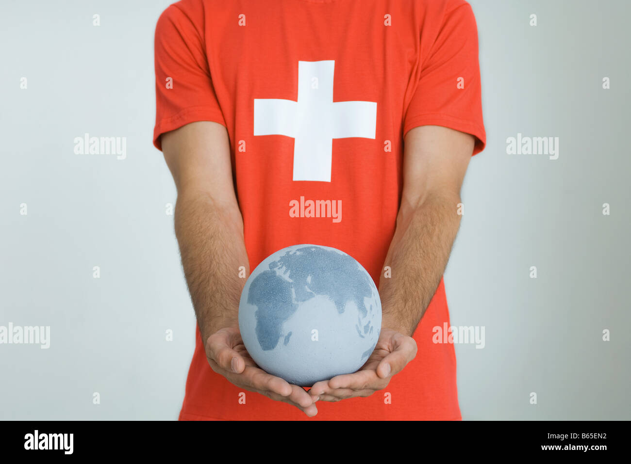 Man wearing Swiss flag tee-shirt, holding globe with both hands Stock Photo